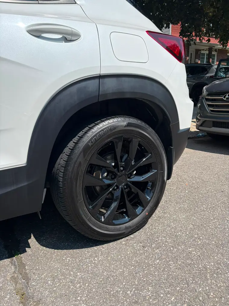 Gloss black wheel and dressed tire on a white Chevrolet Trailblazer after a wheel detail